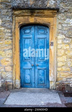 Eine Steinmauer mit einer alten blauen Tür in der Mitte des Rahmens. Die warmen Ziegelsteine und Steine lassen im Bild Platz für Text. Stockfoto