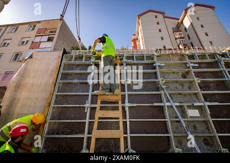 Blick von hinten auf den Bauarbeiter mit Sicherheitsweste und gelbem Helm, wie stehend auf Holzleitern verstellbar, Montage hohe abnehmbare große Form. Stockfoto