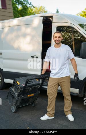 Lächelnder kaukasischer Arbeiter in den 40er Jahren, der seine Werkzeugkästen in seinen Lieferwagen verladen hat. Thema „Business Vehicles“. Stockfoto