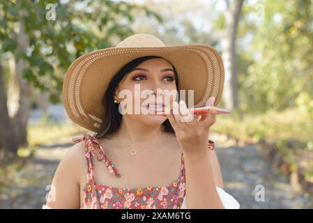 Frau, die Audio auf Handy aufnimmt, mit Sonnenhut. Außenporträt, sonniger Tag. Stockfoto