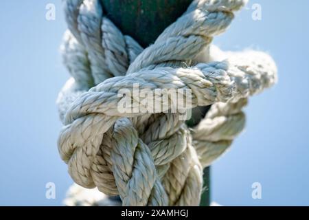 Nahaufnahme eines verwitterten Seils, das in einem Knoten um einen Metallpfosten gebunden ist. Stockfoto