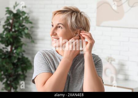 Reife Frau, die im Zimmer Hörgerät auf das Ohr legt Stockfoto