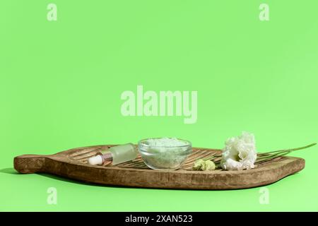 Holzplatte mit natürlichem Körperpeeling, ätherischem Öl und Blumen auf grünem Hintergrund Stockfoto