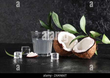 Hälften frischer Kokosnuss mit Glas Wasser und Eiswürfeln auf schwarzem Hintergrund Stockfoto