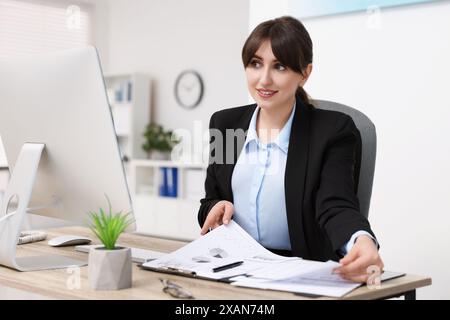 Lächelnde Sekretärin macht Papierkram am Tisch im Büro Stockfoto