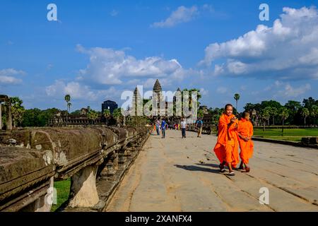 Mönche in orangefarbenen Gewändern wandern in Angkor Wat, Kambodscha, unter einem leuchtend blauen Himmel, umgeben von alter Tempelarchitektur und Palmen. Stockfoto