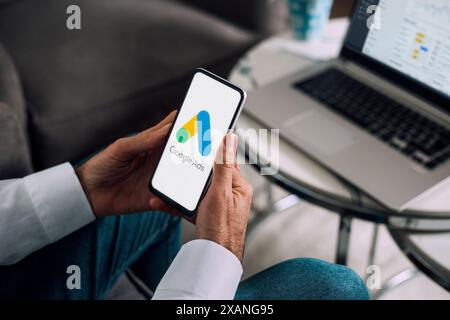 Mann, der ein Mobiltelefon mit Google Ads auf dem Bildschirm und im Hintergrund einen Computer mit Anzeigenstatistiken verwendet. Rosario, Argentinien - 5. Juni 2024. Stockfoto