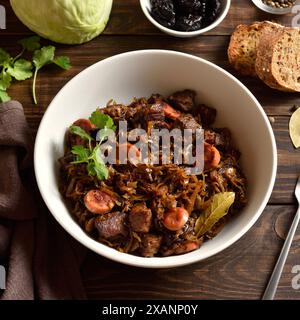 Gedünsteter Kohl (polnische Bigos) mit Sauerkraut, Pilzen, Räucherfleisch und Gewürzen in einer weißen Keramikschale auf Holztisch. Nahansicht Stockfoto