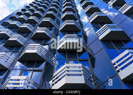 Weitwinkelblick nach oben auf ein modernes Gebäude mit geometrischer Fassade mit weißen Balkonen und reflektierenden blauen Glasfenstern, die weiß c reflektieren Stockfoto