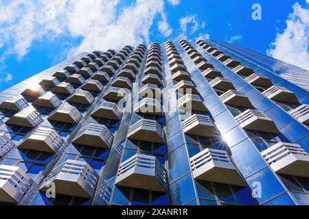 Blick nach oben auf einen Wolkenkratzer mit moderner Architektur mit geometrischen Balkonen und reflektierender Glasfassade. Stockfoto