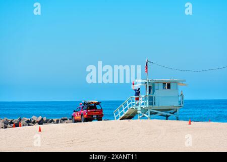 Los Angeles, Kalifornien - 3. April 2024: Rettungsschwimmerturm am Venice Beach mit dem legendären roten Rettungsschwimmerwagen, der neben ihm geparkt wird Stockfoto