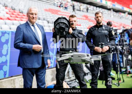 07. Juni 2024, Bayern, München: Einsatzkräfte der Technischen Task Force der Sonderpolizeieinheiten demonstrieren einen UAV-Störsender (UAV = unbemanntes Luftfahrzeug) zur Verteidigung gegen Drohnen auf einer Pressekonferenz zur Vorstellung des Sicherheitskonzepts für die Fußball-Europameisterschaft in der Münchner Fußball-Arena in München (Bayern) am 7. Juni 2024. Joachim Herrmann (CSU), bayerischer Innenminister, steht daneben und beobachtet die Demonstration. Der Jammer kann benutzt werden, um die Kontrolle über eine eindringende Drohne zu übernehmen, damit sie zur Landung gezwungen werden kann. Die Fußball-Europameisterschaft beginnt Stockfoto