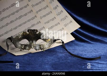 Elegante Gesichtsmaske und Notenblätter auf blauem Stoff. Theateraufführung Stockfoto