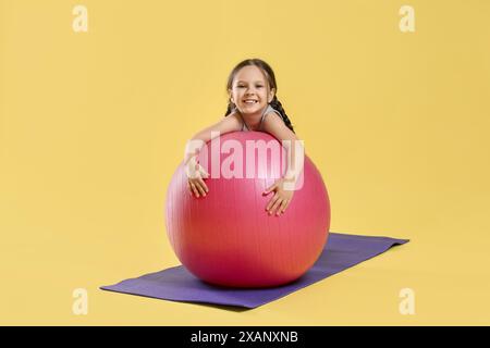 Süßes kleines Mädchen mit passendem Ball auf gelbem Hintergrund Stockfoto