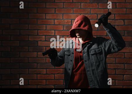 Dieb im Hoodie mit Pistole und Taschenlampe an der roten Ziegelwand Stockfoto