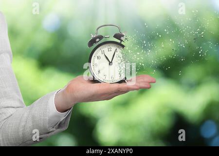 Die Zeit wird knapp. Frau mit auflösendem Wecker auf verschwommenem Hintergrund, Nahaufnahme Stockfoto