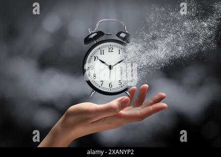 Die Zeit wird knapp. Frau mit auflösendem Wecker auf verschwommenem Hintergrund, Nahaufnahme Stockfoto