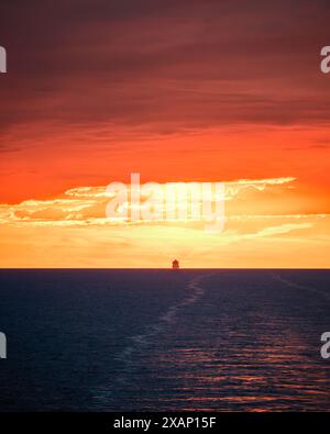 Ein großes Schiff, das am Horizont des Mittelmeers vor einem dramatischen orangen Sonnenuntergang eine Silhouette bildet Stockfoto