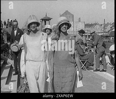 Zwei weibliche Zivilisten, die intelligente Outfits tragen, gehen in einem Pferderennen auf die Kamera zu, 1920er Aus „Time to Remember – Teenage Flapper“, 1920er Jahre (Reel 2); ein Dkumentary über das Leben von Frauen in den 1920er Jahren – großartiger Kommentar von Joyce Grenfell. Stockfoto