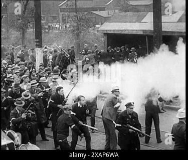 Kleine Menge amerikanischer Zivilisten bei Demonstration/Streik im Konflikt mit der Polizei, Schüsse werden abgefeuert, 1930er Jahre Eine Gruppe von Männern vor einem Stahlwerk, die bewaffnete Polizisten gegenüberstehen. Aus Time to Remember - The Tough Guys, 1930er Jahre (Reel 1); ein Dokumentarfilm über das Leben in Amerika, das von Depressionen und Gangstern heimgesucht wurde. Stockfoto