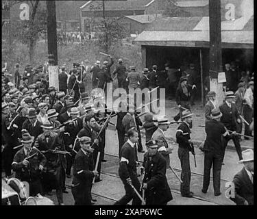 Kleine Menge amerikanischer Zivilisten auf Demonstration/Streik im Konflikt mit der Polizei, 1930er Jahre Männer mit Waffen vor einem Stahlwerk. Aus Time to Remember - The Tough Guys, 1930er Jahre (Reel 1); ein Dokumentarfilm über das Leben in Amerika, das von Depressionen und Gangstern heimgesucht wurde. Stockfoto