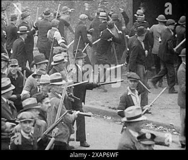 Kleine Menge amerikanischer Zivilisten auf Demonstration/Streik im Konflikt mit der Polizei, 1930er Jahre Eine Gruppe von Männern vor einem Stahlwerk, die bewaffnete Polizisten gegenüberstehen. Aus Time to Remember - The Tough Guys, 1930er Jahre (Reel 1); ein Dokumentarfilm über das Leben in Amerika, das von Depressionen und Gangstern heimgesucht wurde. Stockfoto