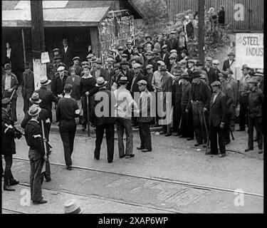 Kleine Menge amerikanischer Zivilisten auf Demonstration/Streik, 1930er Jahre Eine Gruppe von Männern vor einem Stahlwerk, die bewaffnete Polizisten gegenüberstehen. Aus Time to Remember - The Tough Guys, 1930er Jahre (Reel 1); ein Dokumentarfilm über das Leben in Amerika, das von Depressionen und Gangstern heimgesucht wurde. Stockfoto