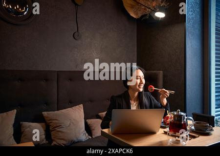 Junge Frau isst Sushi und arbeitet an einem Geschäftsprojekt auf Laptop Stockfoto