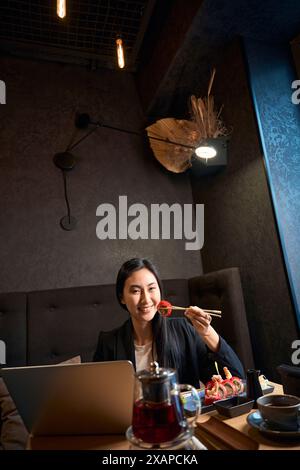 Fröhliche asiatische Frau, die köstliches Sushi im japanischen Restaurant genießt Stockfoto