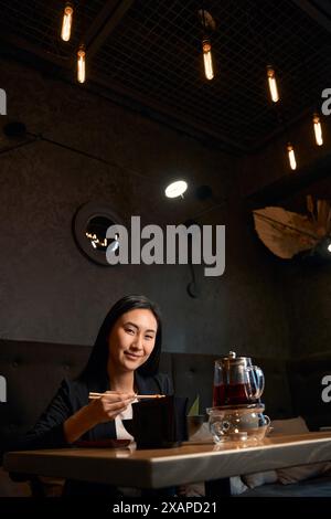 Hübsche asiatische Frau posiert vor der Kamera mit einem Lächeln und Essen draußen Stockfoto