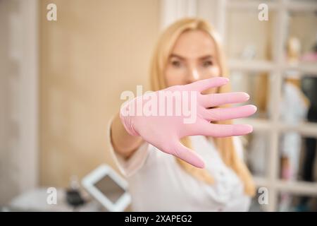 Arzt im Einweg-Nitrilhandschuh mit Stop-Geste im Büro Stockfoto