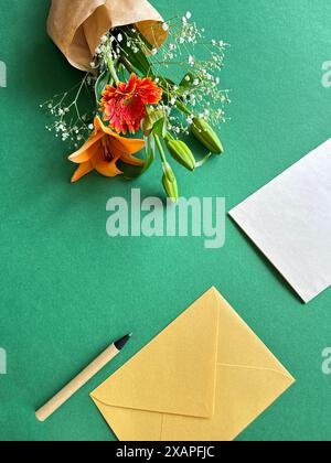 Lebendiger Blumenstrauß mit Umschlag und Stift auf grünem Hintergrund Stockfoto