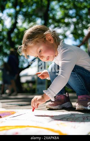 Mädchen malte draußen. Glückliches Kind zieht im Park. Ein kleines Mädchen zeichnet im Park mit Buntstiften auf Papier. Stockfoto