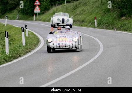 Ein silberner Oldtimer-Rennwagen wird von einem Beifahrer nach draußen geschwenkt, begleitet von einem anderen Oldtimer, Oldtimer, Autorennen, Mille Miglia, 1000 Miglia Stockfoto