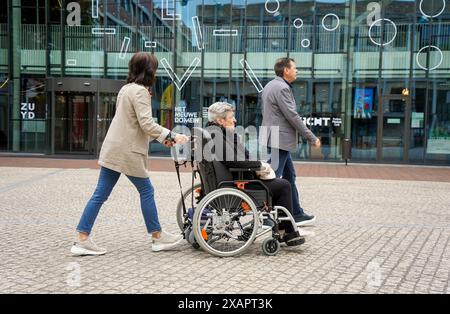 Frau schiebt Rollstuhl mit älteren Frauen und Männern dahinter. Stockfoto
