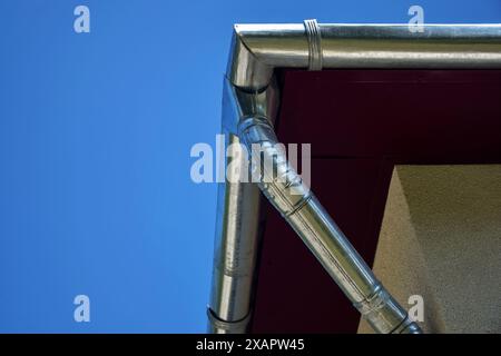 Teil des Dachs mit verzinktem Rohr und Regenrinnen zum Ablassen des Regenwassers. Ansicht von unten vor blauem Himmel und Sonnenblendung. Nahaufnahme. Stockfoto