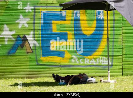 08. Juni 2024, Hessen, Frankfurt/Main: Ein Mann macht ein Nickerchen vor einem "EU"-Graffiti am Rande der bundesweiten Demonstration "V.O.T.Y. - Abstimmung des Jahres" in Frankfurt. Ein bundesweites Bündnis der Zivilgesellschaft fordert die Demonstration. Foto: Boris Roessler/dpa Credit: dpa Picture Alliance/Alamy Live News Stockfoto