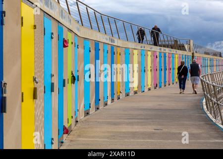 Milford on Sea, Hampshire, Großbritannien. Juni 2024. Wetter in Großbritannien: Sonnige Intervalle in Milford-on-Sea, Hampshire, Großbritannien. Die Leute genießen einen Spaziergang entlang der Promenade an bunten Strandhütten vorbei. Quelle: Carolyn Jenkins/Alamy Live News Stockfoto