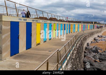 Milford on Sea, Hampshire, Großbritannien. Juni 2024. Wetter in Großbritannien: Sonnige Intervalle in Milford-on-Sea, Hampshire, Großbritannien. Die Leute genießen einen Spaziergang entlang der Promenade an bunten Strandhütten vorbei. Quelle: Carolyn Jenkins/Alamy Live News Stockfoto