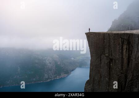 Ein einsamer Wanderer steht am Rande von Preikestolen, einer dramatischen Klippe mit Blick auf einen nebeligen Fjord in Norwegen. Preikestolen Norwegen Stockfoto