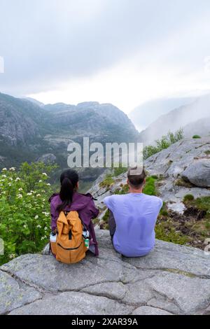 Zwei Personen sitzen auf einer felsigen Klippe mit Blick auf einen atemberaubenden norwegischen Fjord und genießen die atemberaubende Aussicht und die friedliche Atmosphäre. Ein Paar wandert durch die Preikestolen, Norwegen Stockfoto