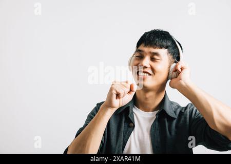 Porträt Asiatisch lächelnder junger Mann, der Hände trägt, die aussehen lassen wie ein Mikrofon halten und ein Lied singen Stockfoto