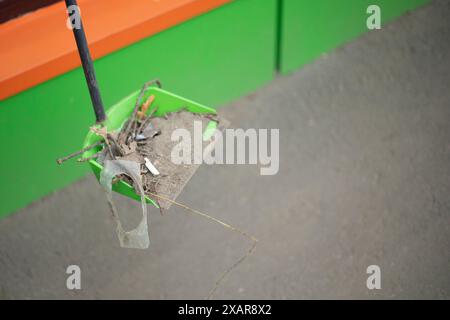 Den Müll auf der Straße aufräumen. Löffel mit Feuer. Besen zum Kehren. Reinigen des Pfads. Stockfoto