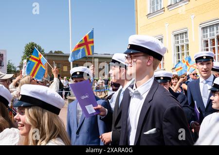 SCHÜLER, DIE DIE SCHULE ZUM LETZTEN MAL VERLASSEN, CELEBRATION, Åland, FINNLAND: Die neuen Absolventen kommen zum letzten Mal aus ihrer Schule, um einen ausgelassenen Empfang von Freunden und Familien zu feiern, die sich vor dem Hauptschulgebäude zum Åland-Abschlussfeiertag 2024 im Åland Lyceum (Ålands Gymnasium) in Mariehamn, Åland Archipel, versammelt haben. Ostsee, Finnland – an diesem Tag verlassen die Schüler die Schule zum letzten Mal. Im Rahmen dieser nordischen Tradition werden Plakate mit Babybildern der Absolventen hochgehalten, und die Studenten tragen ihre Studentmössa im Matrosenstil und kleiden sich in Anzug Stockfoto