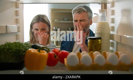 POV-Perspektive vom Inneren des Kühlschranks Erwachsenes Paar fühlte sich schlecht ekelhaft unangenehmer Geruch vom kaputten Kühlschrank verdorbenes verfaultes Essen in der Mitte Stockfoto