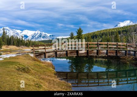 Holzbogen Fußgängerbrücke in Cascade Teiche Park im Herbst sonnigen Tag, schneebedeckten Mount Astley Reflexion auf der Wasseroberfläche. Banff National Park Stockfoto