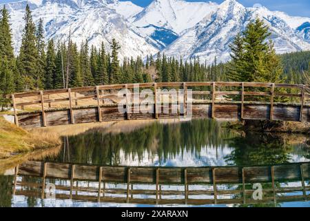 Holzbogen Fußgängerbrücke in Cascade Teiche Park im Herbst sonnigen Tag, schneebedeckten Mount Astley Reflexion auf der Wasseroberfläche. Banff National Park Stockfoto