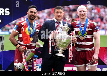 Matt Peet, Cheftrainer der Wigan Warriors (Mitte), posiert mit der Trophäe, Spieler Bevan French (links) mit der Trophäe „Mann des Matches“ und Liam Farrell feiern nach der letzten Pfeife im Finale des Betfred Challenge Cup im Wembley Stadium, London. Bilddatum: Samstag, 8. Juni 2024. Stockfoto