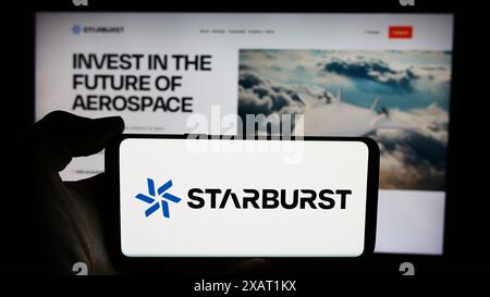 Person, die ein Mobiltelefon mit dem Logo der US-amerikanischen Risikokapitalgesellschaft Starburst Aerospace Ltd. Vor der Webseite des Unternehmens hält. Schwerpunkt auf dem Display des Telefons. Stockfoto