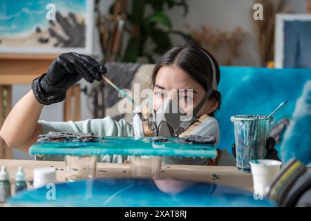 Eine fokussierte, aufmerksame Künstlerin, die Epoxidkunstwerke kreiert, arbeitet die Details der Malerei gründlich aus Stockfoto